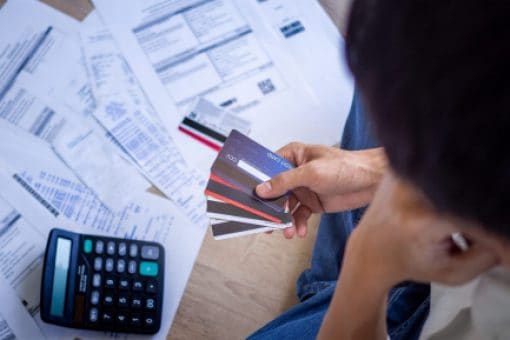 A person sits on the floor holding credit cards in their hand with scattered papers and a calculator.