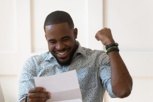 Man sitting at a desk, smiling and pumping his fist as he reads his tax return.