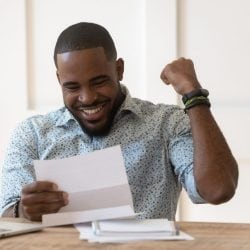 Man sitting at a desk, smiling and pumping his fist as he reads his tax return.