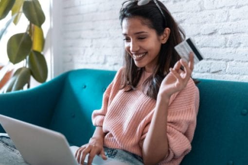 Young woman shopping online with a credit card and laptop while sitting on a sofa.