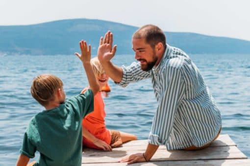 A man plays with two small children by a lake.