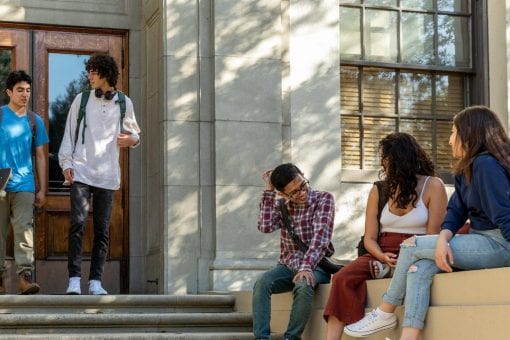 College students are standing and sitting outside of a building.