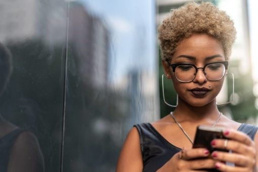 Young woman types on her mobile phone on a sunny city street.