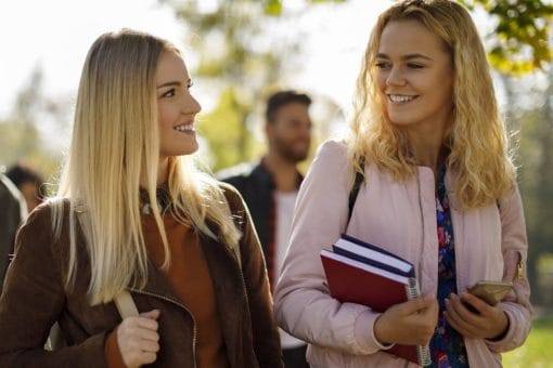 Young women smile and look at one another as they walk outside