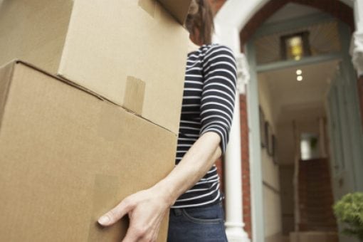 Woman carrying cardboard boxes in front of an open door to a house.