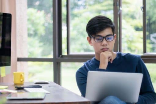 Young man sits at his desk and looks thoughtfully at his laptop