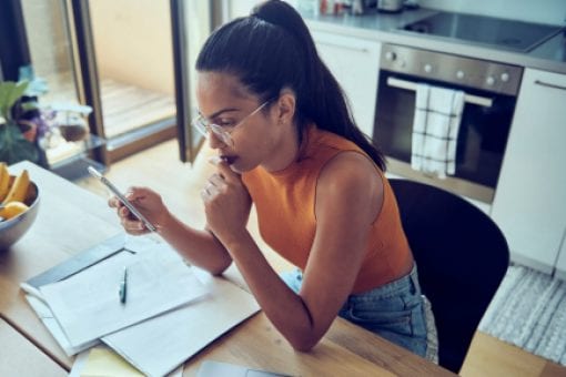 Young woman sits at kitchen table looking at a phone.