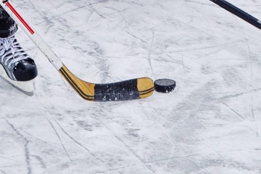 Closeup of hockey skate, stick and puck on ice.