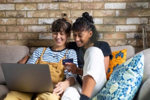 Woman holds a credit card and looks at a laptop screen with her partner.