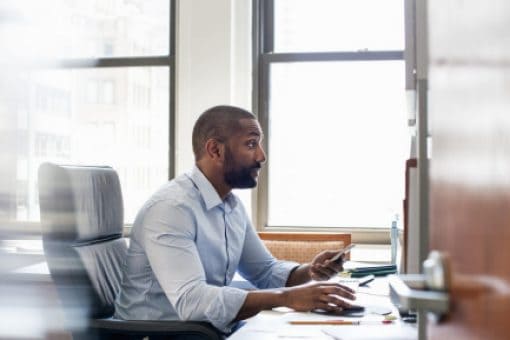 Man using laptop looks at credit card in his hand