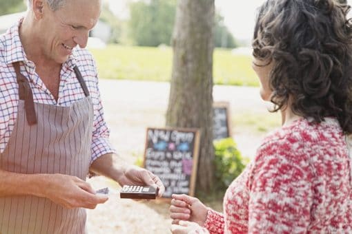 A woman hands her credit card to a shop owner holding a card terminal.