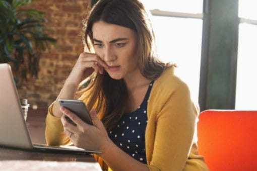 Worried woman bites her nail as she looks at her phone.