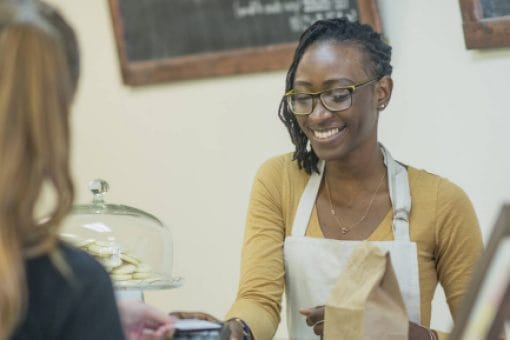 A store clerk holds a card reader as a woman pays with a contactless credit card.