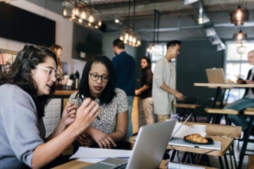 Two women look at laptop in café.