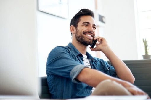 Happy man sits on a couch talking on his phone.