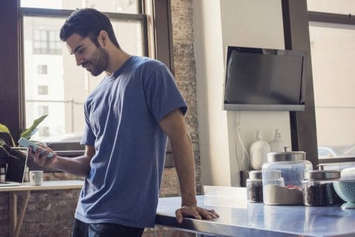 Man in his kitchen smiles looking down at his phone
