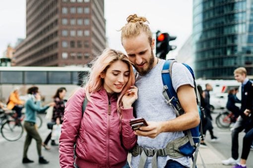 A happy traveling couple on a busy street look at the man’s mobile phone