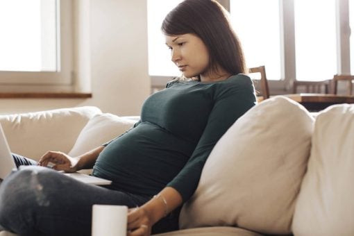 Woman sits alone on a couch looking at laptop.