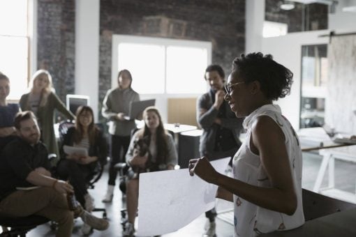 Woman holds up paper in front of a group of coworkers in an office.