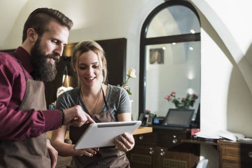 Two restaurant workers look at a digital tablet.