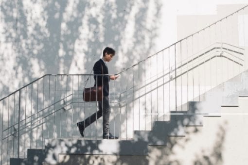 Professional man with a leather messenger bag climbs an outdoor staircase.