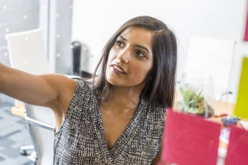 A woman at work reviews sticky notes on a clear board.