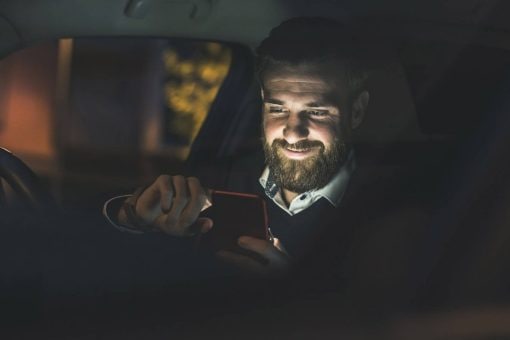 Man smiles at mobile phone in a car
