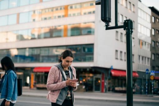 A woman looks at her mobile phone on a city street corner.
