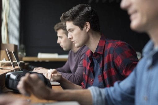 Three individuals sit by one another each looking at a laptop screen.