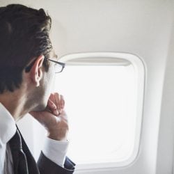 Man in suit looks out airplane window.
