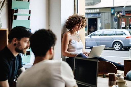 Two men and a woman using laptops in a cafe.