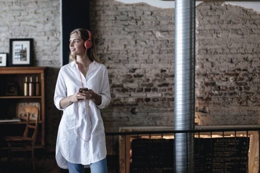 A woman with headphones holds her phone while standing in a rustic building.