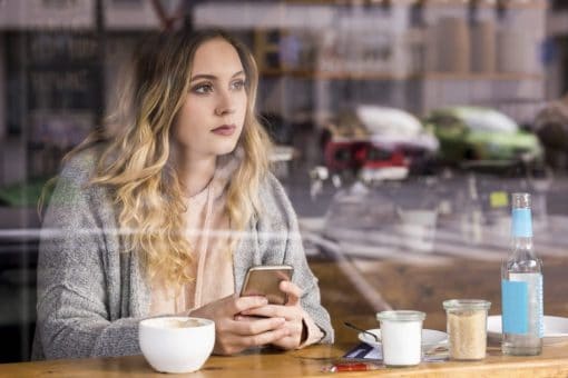 Woman sits in restaurant looking out window and holding mobile phone.
