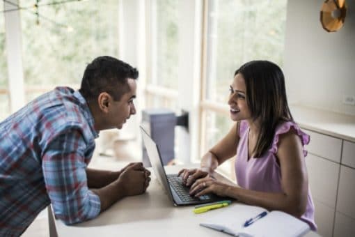 Couple speaks to one another as the woman types on a laptop