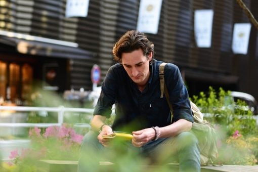 A man sits in a garden holding a yellow notebook.