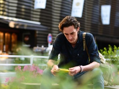 A man sits in a garden holding a yellow notebook.