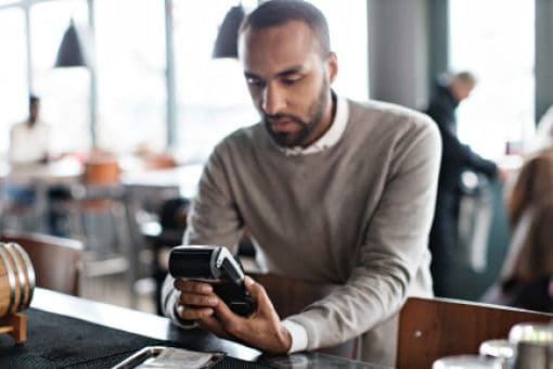 Restaurant customer holds credit card reader in his hands to pay his bill.