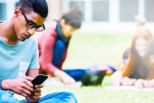 A student sits in the college square and looks through their cell phone.