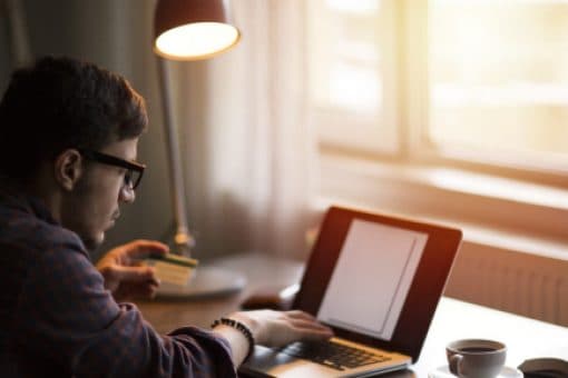 Man working at desk on laptop with a notepad, pen, and coffee mug nearby.