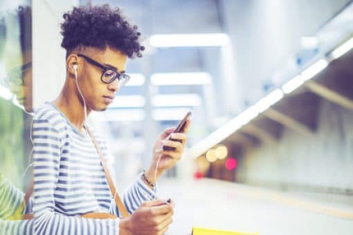Man wearing headphones and looking at his phone on a subway platform. 