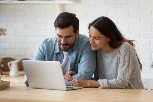 Happy couple sits together as they look at the screen of their laptop
