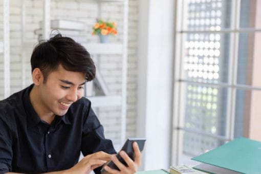 Young, happy man uses a calculator as he sits at a desk.