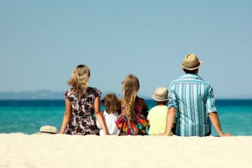 A couple and their three kids sit on the sand at a beach looking at the ocean.