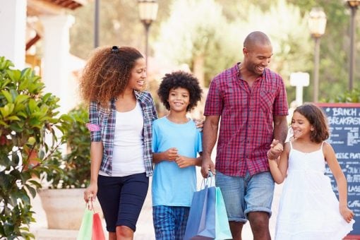 A family carrying shopping bags walks down a sidewalk together.