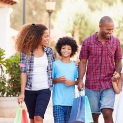 A family carrying shopping bags walks down a sidewalk together.