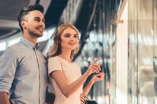 A young couple window shops as the woman points at the bright store glass.