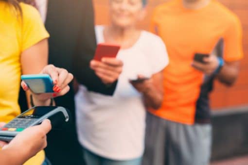 People in line use their phone to tap a credit card reader.