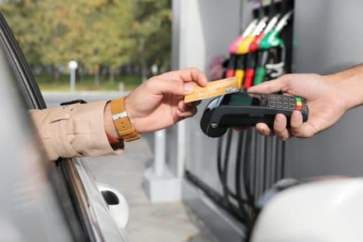 A driver uses their credit card at a gas pump to pay for gas and earn rewards.