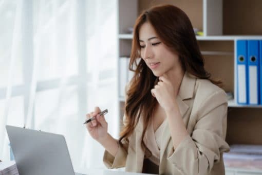 Professional woman holds a pen as she works on laptop