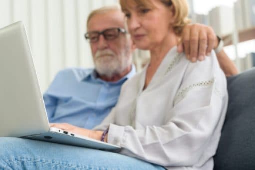 Senior couple using laptop sitting on a couch.